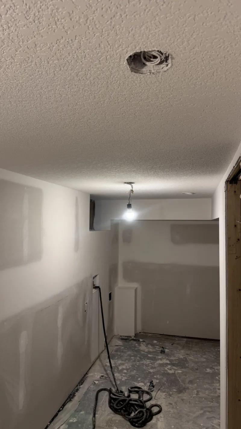 Basement drywall finishing with textured ceiling and recessed light openings in Calgary home renovation project.